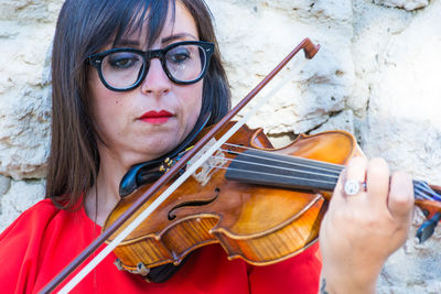 Close-up of woman playing violin against stone wall
