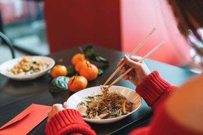 Beautiful young woman in red clothes eating noodles with bamboo chopsticks in chinese restaurant