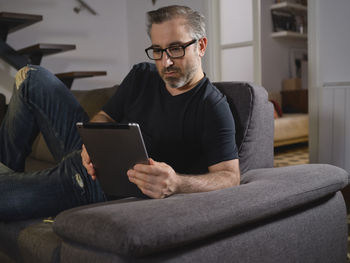 Relaxed man talking on the tablet serious alone on the sofa in the living room at home