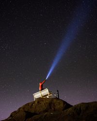 Low angle view of man with flashlight against sky at night