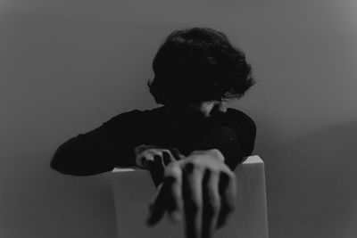 Rear view of woman sitting against wall at home