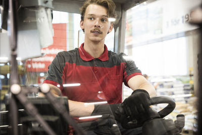 Young male warehouse worker driving forklift in warehouse seen through windshield