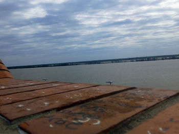 Wooden pier on calm sea against cloudy sky