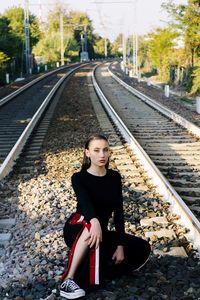 Portrait of young woman sitting on railroad track