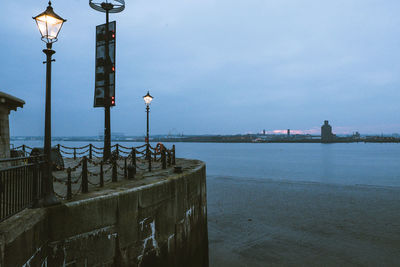 Illuminated street light by sea against sky