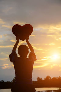 Silhouette woman with arms raised standing against sky during sunset