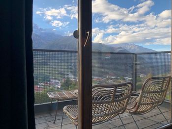 Empty chairs and tables against sky seen through window