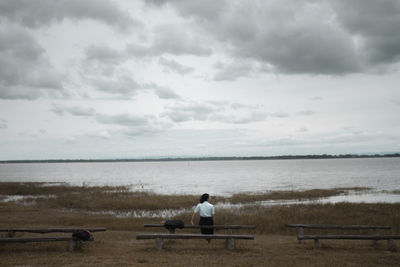 Rear view of man sitting on bench against sea