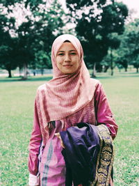 Portrait of smiling young woman wearing hijab while standing in public park