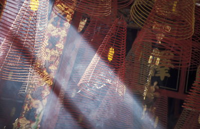 Low angle view of sunlight streaming by spiral incense sticks in temple