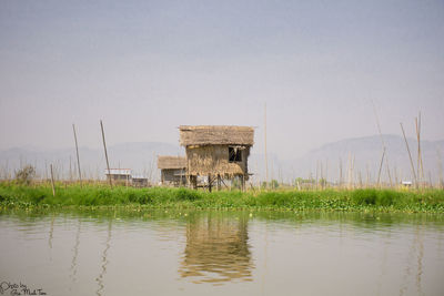 Stilt houses on field by lake against sky