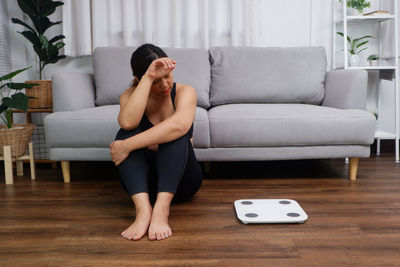 Asian women sitting on floor and looking at body weight scale, planning on body weights control