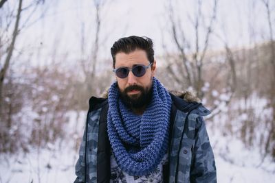Portrait of man wearing sunglasses standing in forest during winter