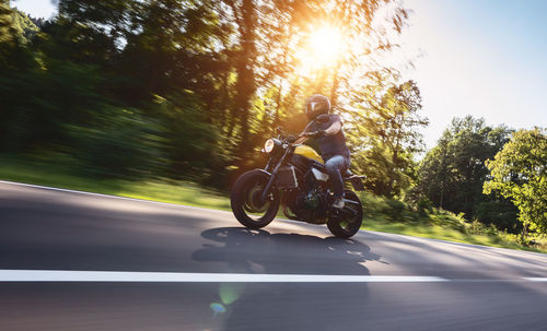 Low angle view of man riding motorcycle on road against trees