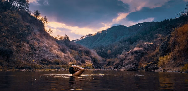 Man in lake against sky during sunset