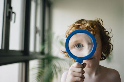 Portrait of shirtless boy playing with magnifying glass at home