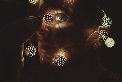Close-up of man wearing chain of lights against black background