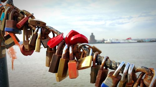 Close-up of padlocks on railing by river against sky