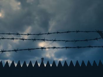 Silhouette barbed wire fence against sky