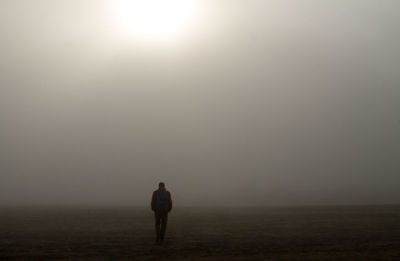 Rear view of silhouette man standing on landscape during foggy weather