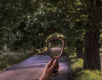 Road and trees reflecting in mirror held by woman