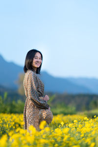 Woman standing by yellow flower on field against sky