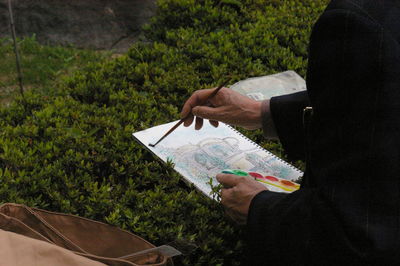 Midsection of man painting in book on field