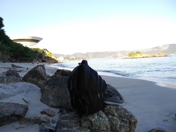 Rear view of people sitting on rock by sea against clear sky