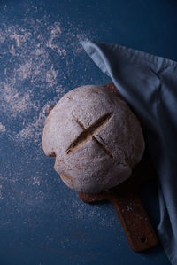 Fresh bread displayed on wood with a tablecloth on a blue background.