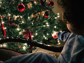 Man sitting on illuminated christmas tree at home