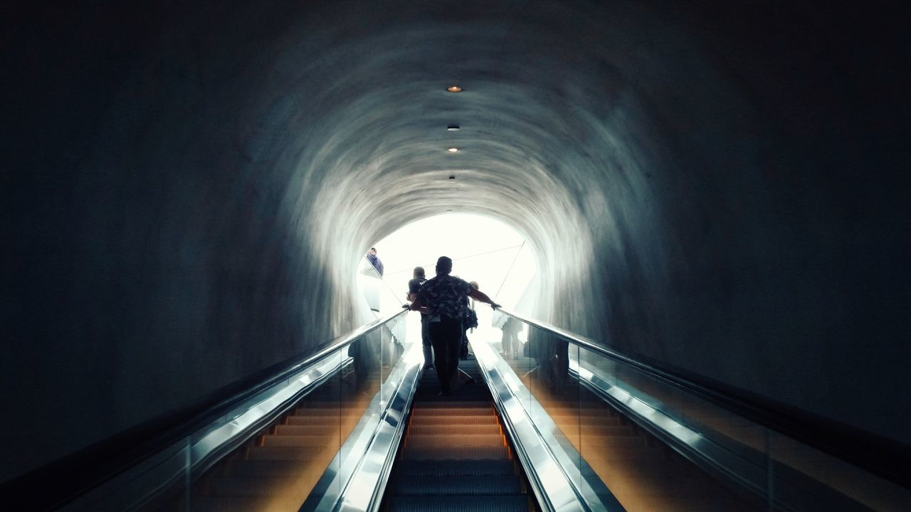 indoors, tunnel, the way forward, light at the end of the tunnel, arch, full length, architecture, rear view, built structure, walking, diminishing perspective, men, lifestyles, railing, illuminated, standing, silhouette, vanishing point