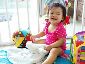 Portrait of cute baby girl sitting by toys on bed at home