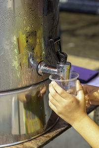 Cropped image of child filling water in plastic cup from faucet