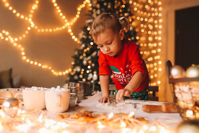 A little girl in red pajamas cooks and eats christmas cookies in the decorated kitchen of the house