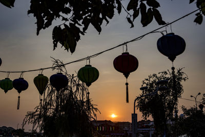Low angle view of lanterns hanging against sky at sunset