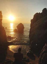Silhouette of man sitting on cliff by sea against clear sky