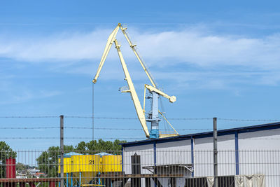 A samll port crane on rails standing on the loading yard, visible yellow silos.