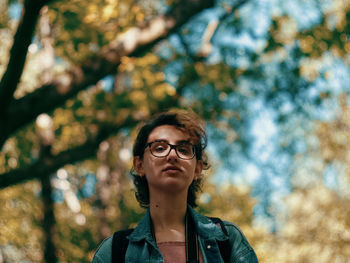 Low angle portrait of young woman standing against trees