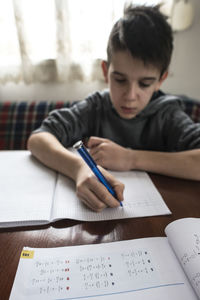 Boy writing in book while sitting on table