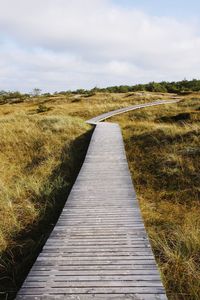 Boardwalk amidst field against sky