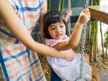 Midsection of mother holding daughter sitting on swing outdoors