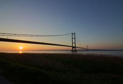 Suspension bridge over river against sky during sunset