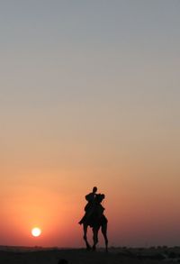 Silhouette man riding camel at desert against sky during sunset