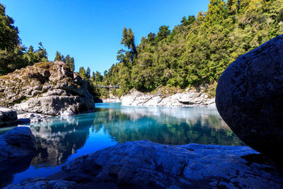 Scenic view of river by mountains against clear blue sky