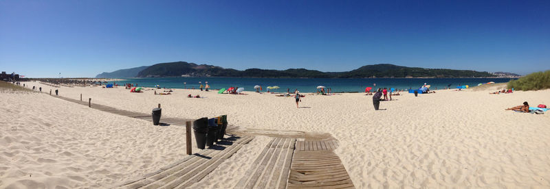 Panoramic view of people on beach against clear blue sky