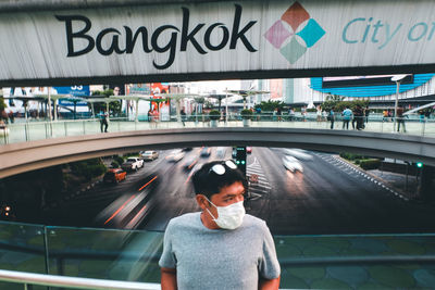 Mid adult man wearing flu mask while standing on footbridge over road in city