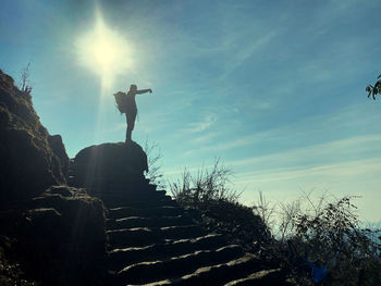 Low angle view of person standing on rock against sky