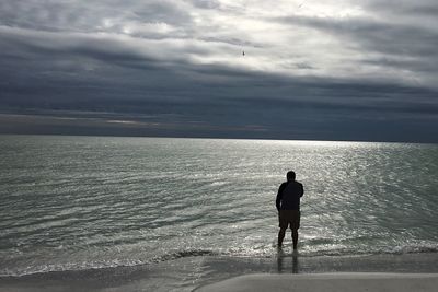 Rear view of silhouette man standing at beach against sky