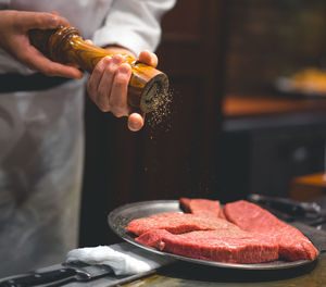 Midsection of chef seasoning salt on meat