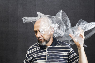 Mature man with a transparent plastic bag flying over his head and face. 